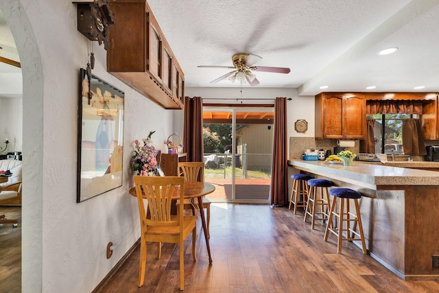 kitchen featuring backsplash, a kitchen bar, ceiling fan, dark wood-type flooring, and a textured ceiling