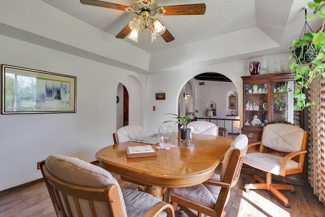 dining room featuring ceiling fan, hardwood / wood-style flooring, a raised ceiling, and a textured ceiling