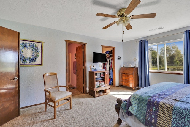 carpeted bedroom featuring ensuite bathroom, a walk in closet, a textured ceiling, a closet, and ceiling fan