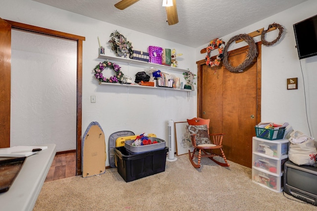 recreation room featuring ceiling fan, carpet flooring, and a textured ceiling