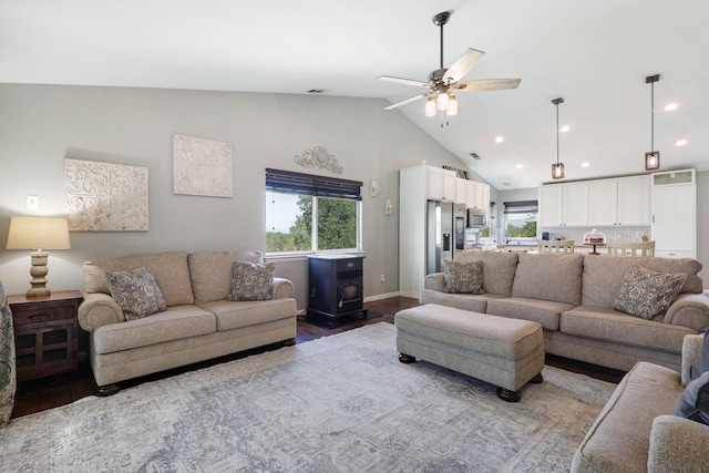 living room featuring wood-type flooring, high vaulted ceiling, ceiling fan, and a wood stove