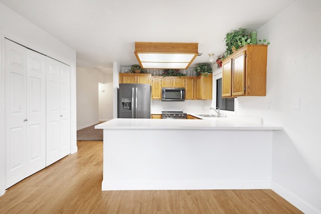 kitchen featuring stainless steel appliances, kitchen peninsula, sink, and light hardwood / wood-style flooring