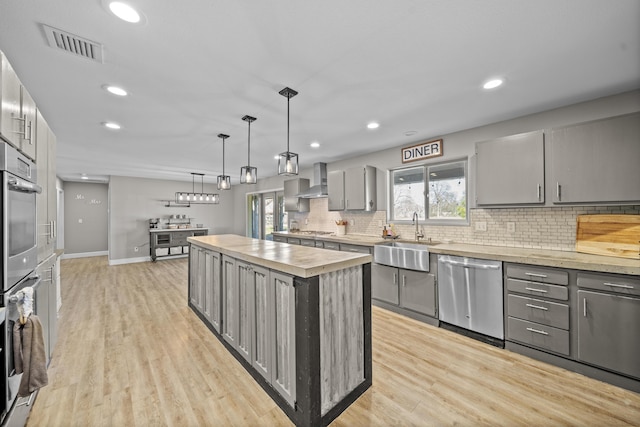 kitchen with a kitchen island, a sink, wall chimney range hood, appliances with stainless steel finishes, and gray cabinets