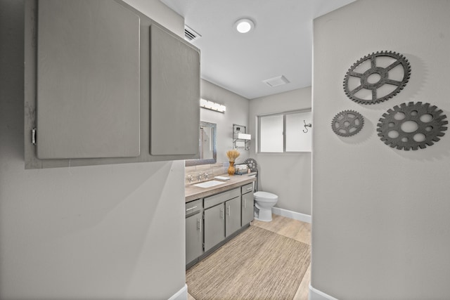 bathroom with baseboards, visible vents, toilet, wood finished floors, and vanity