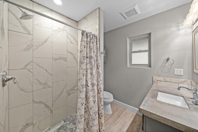 full bathroom with visible vents, toilet, wood finished floors, a tile shower, and vanity