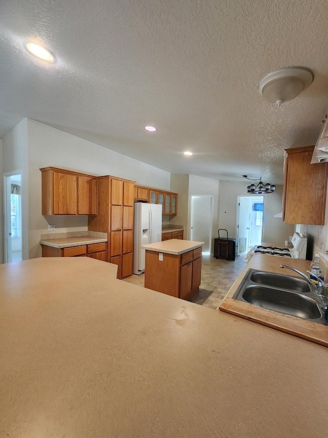 kitchen featuring a kitchen island, range with gas cooktop, sink, white fridge with ice dispenser, and a textured ceiling