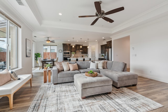 living room with ornamental molding, light hardwood / wood-style floors, and a tray ceiling