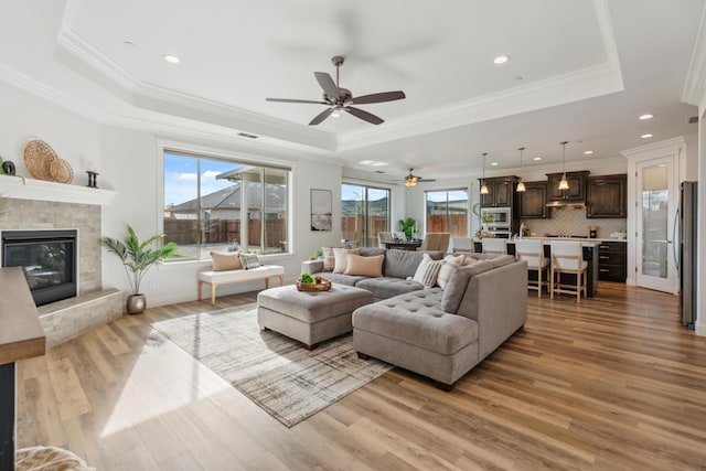 living room with crown molding, light hardwood / wood-style flooring, a tile fireplace, and a raised ceiling