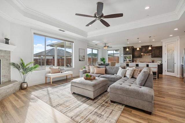 living room featuring a fireplace, ornamental molding, a tray ceiling, and light wood-type flooring