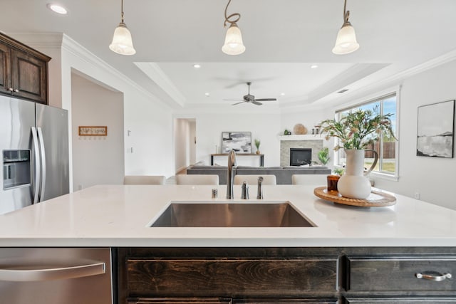 kitchen featuring pendant lighting, sink, dark brown cabinetry, ornamental molding, and a center island with sink