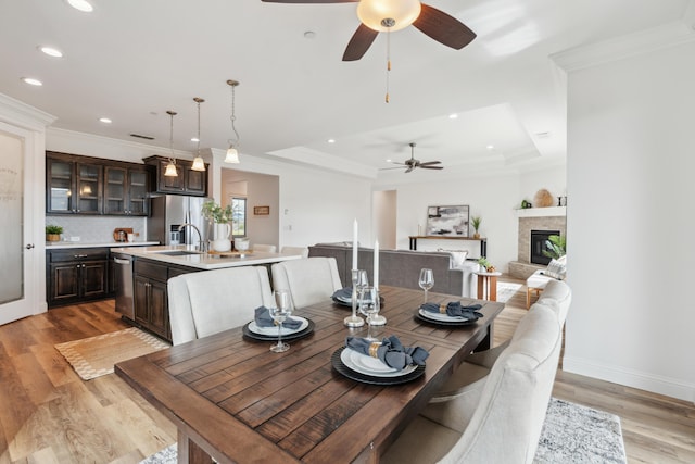 dining area with sink, light hardwood / wood-style flooring, ornamental molding, and a raised ceiling