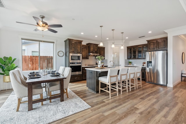 kitchen with stainless steel appliances, dark brown cabinets, a kitchen island with sink, and pendant lighting