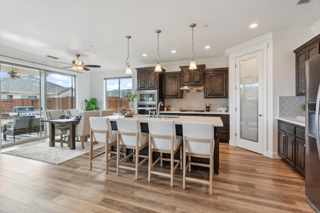 kitchen featuring sink, appliances with stainless steel finishes, a kitchen island with sink, dark brown cabinetry, and light wood-type flooring