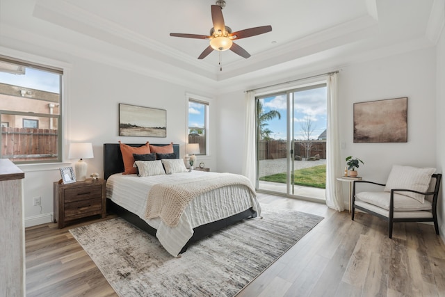 bedroom featuring a tray ceiling, light hardwood / wood-style flooring, and access to outside