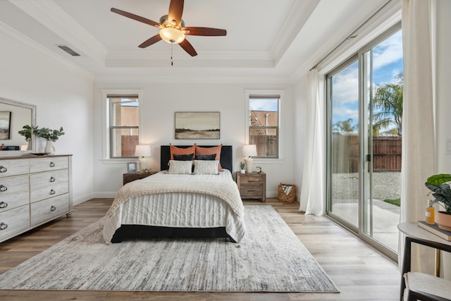 bedroom featuring crown molding, a raised ceiling, light hardwood / wood-style floors, and access to outside