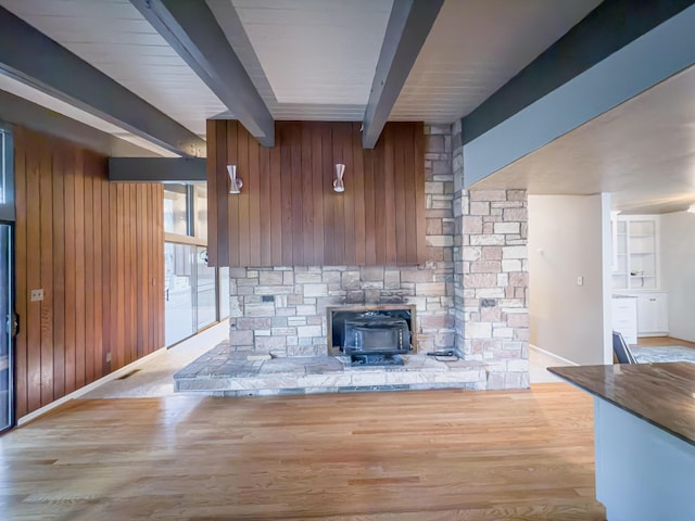 interior space featuring beam ceiling, light hardwood / wood-style floors, a wood stove, and wood walls