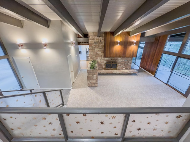 interior space with beamed ceiling, carpet flooring, a stone fireplace, and wood walls