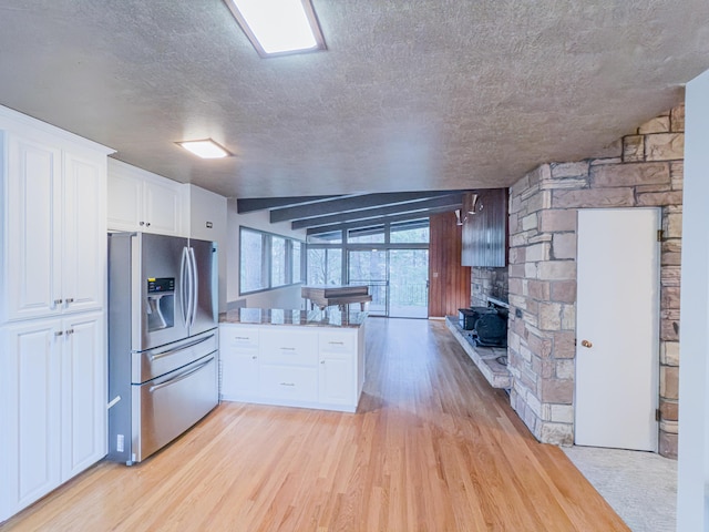 kitchen with a fireplace, white cabinetry, stainless steel fridge, light hardwood / wood-style floors, and a textured ceiling