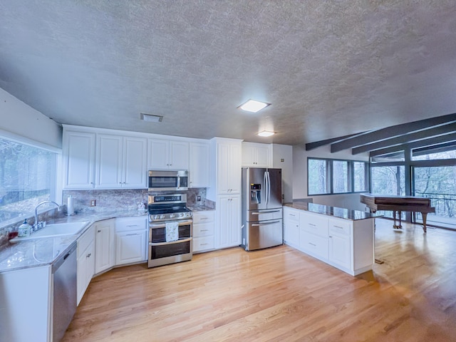 kitchen featuring appliances with stainless steel finishes, sink, white cabinets, decorative backsplash, and light wood-type flooring