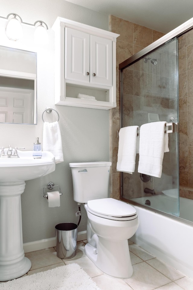 bathroom with baseboards, toilet, tile patterned flooring, combined bath / shower with glass door, and a sink