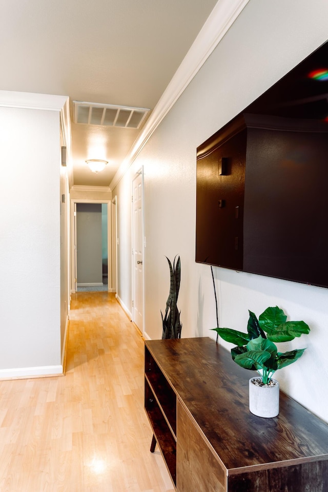 hall featuring light wood-style floors, visible vents, crown molding, and baseboards