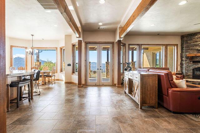 kitchen with french doors, a stone fireplace, hanging light fixtures, a notable chandelier, and beam ceiling