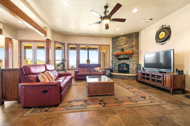 living room with a stone fireplace, ceiling fan, and french doors