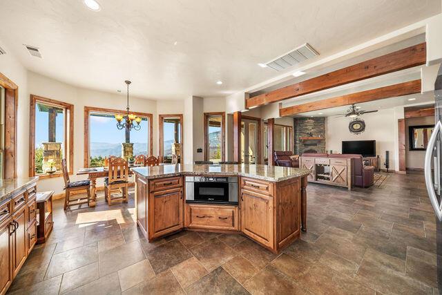 kitchen with ceiling fan with notable chandelier, light stone countertops, a kitchen island with sink, and hanging light fixtures