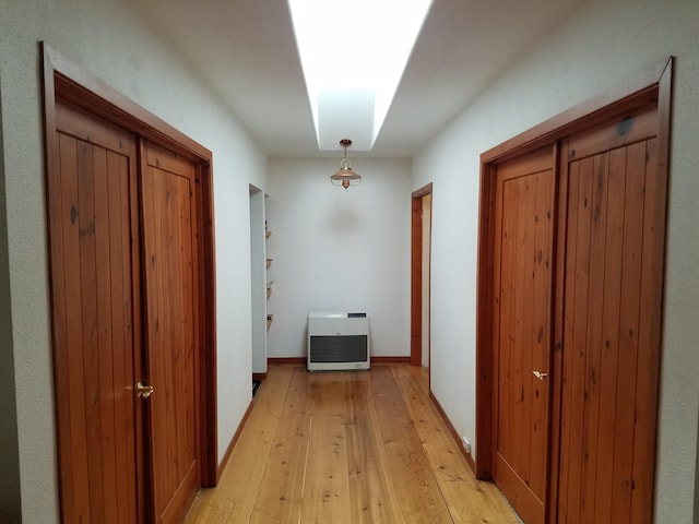 hall featuring light wood-type flooring, baseboards, and heating unit