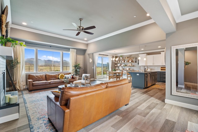 living room featuring ceiling fan with notable chandelier, sink, ornamental molding, a mountain view, and light wood-type flooring