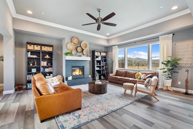 living room with crown molding, a fireplace, light hardwood / wood-style floors, and ceiling fan