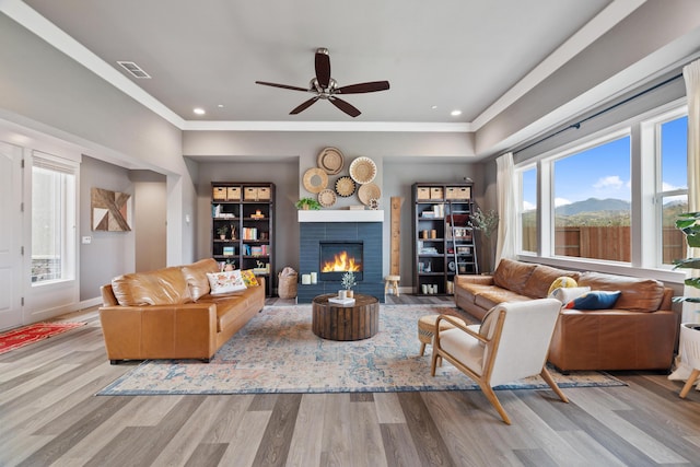 living room with crown molding, a mountain view, ceiling fan, a fireplace, and light hardwood / wood-style floors