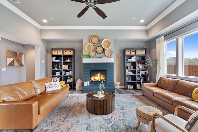 living room with a tile fireplace, wood-type flooring, and ceiling fan