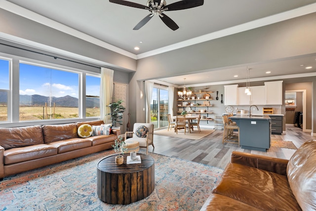 living room featuring sink, light wood-type flooring, ornamental molding, a mountain view, and ceiling fan with notable chandelier