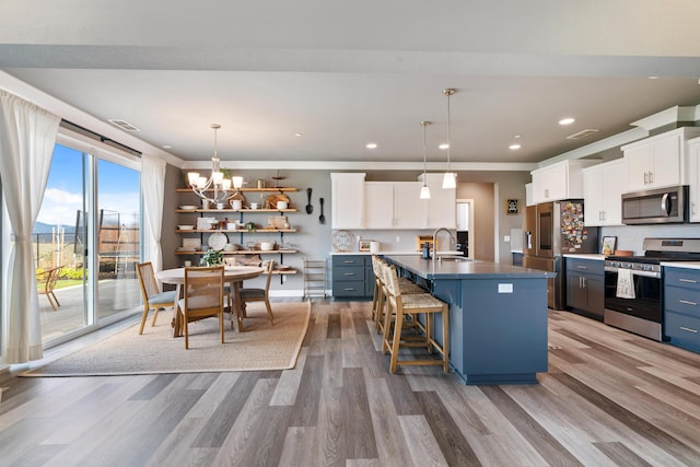 kitchen featuring white cabinetry, an island with sink, appliances with stainless steel finishes, and decorative light fixtures