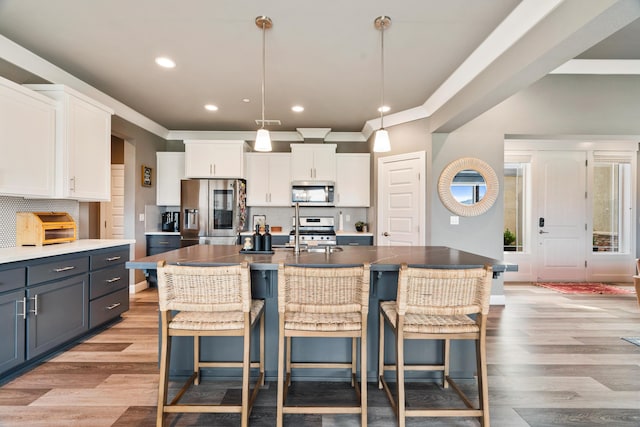 kitchen with a kitchen island with sink, hanging light fixtures, white cabinets, and appliances with stainless steel finishes