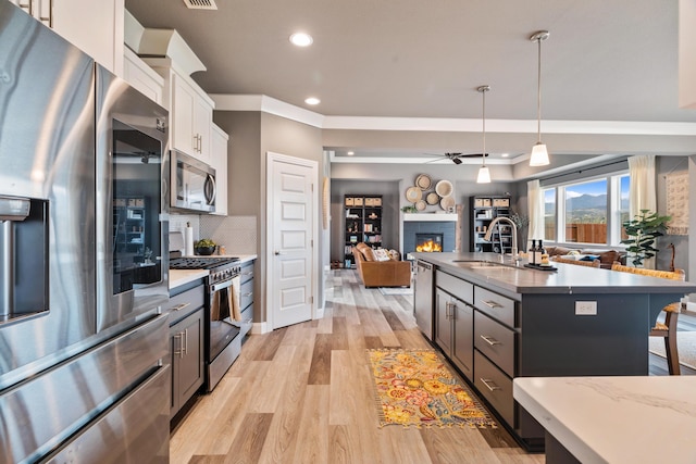 kitchen with sink, pendant lighting, stainless steel appliances, a kitchen island with sink, and white cabinets