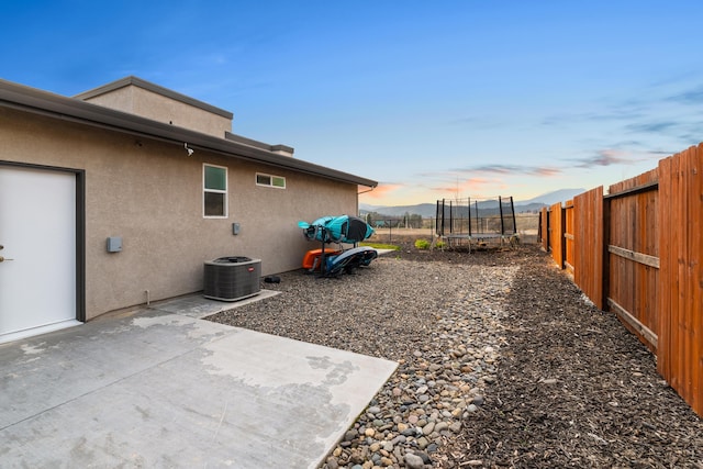 yard at dusk featuring a patio, cooling unit, and a trampoline