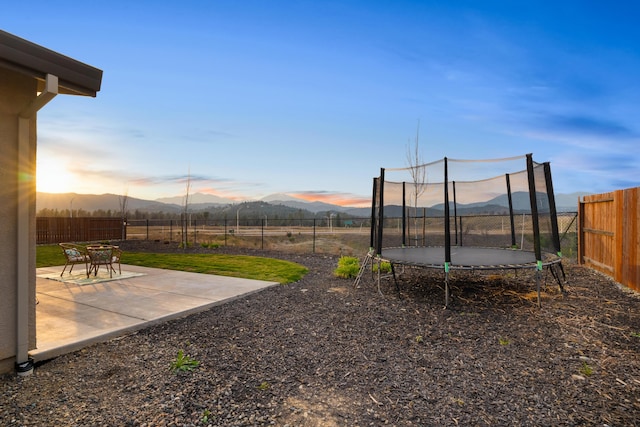 yard at dusk featuring a mountain view, a trampoline, and a patio area