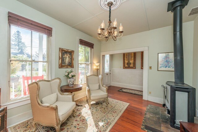 sitting room featuring dark wood-type flooring, plenty of natural light, an inviting chandelier, and a wood stove