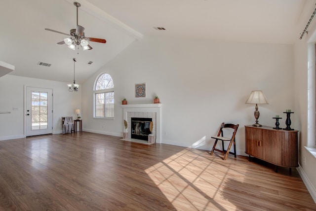 unfurnished living room featuring beam ceiling, ceiling fan with notable chandelier, a tile fireplace, and hardwood / wood-style flooring