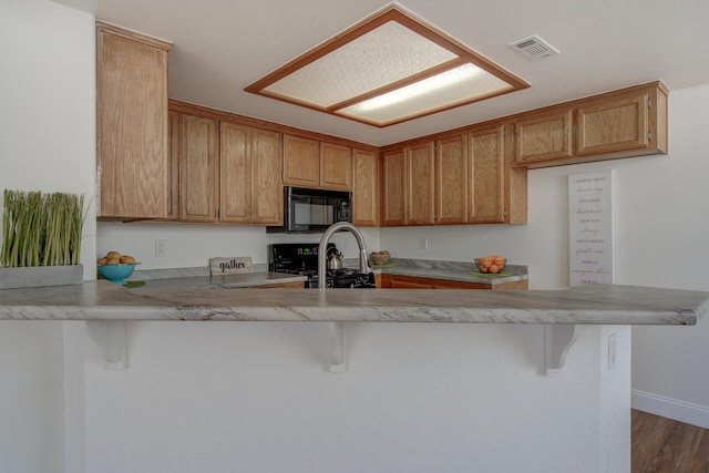 kitchen with hardwood / wood-style floors, range, a kitchen breakfast bar, and kitchen peninsula