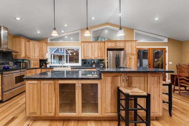 kitchen featuring appliances with stainless steel finishes, sink, hanging light fixtures, a center island, and wall chimney range hood