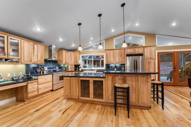 kitchen featuring a kitchen breakfast bar, hanging light fixtures, a center island, stainless steel appliances, and wall chimney range hood