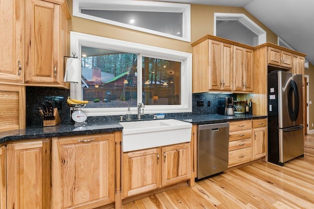 kitchen with vaulted ceiling, appliances with stainless steel finishes, sink, and dark stone counters