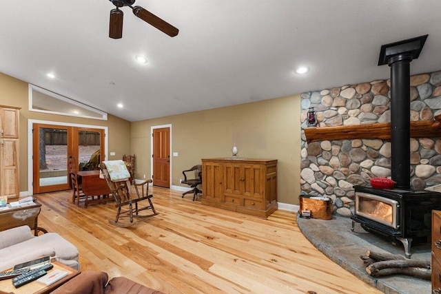 living room featuring a wood stove, ceiling fan, vaulted ceiling, french doors, and light wood-type flooring