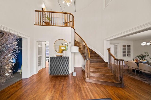 staircase featuring an inviting chandelier, a towering ceiling, and hardwood / wood-style flooring