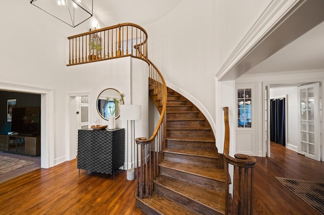 staircase featuring hardwood / wood-style flooring, a towering ceiling, and a notable chandelier