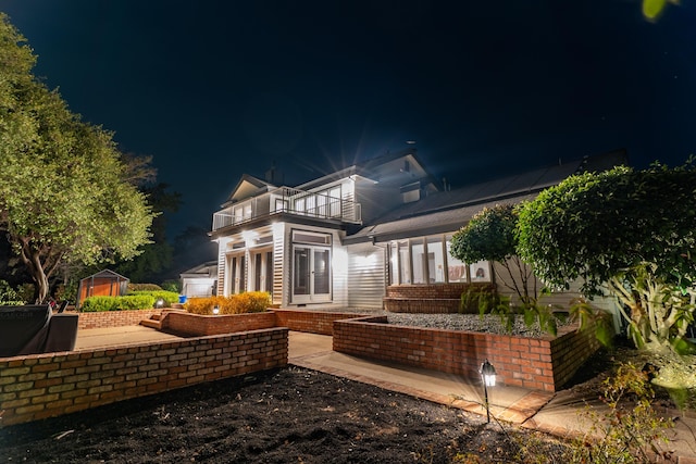 back house at night with a balcony, a storage shed, and a patio area