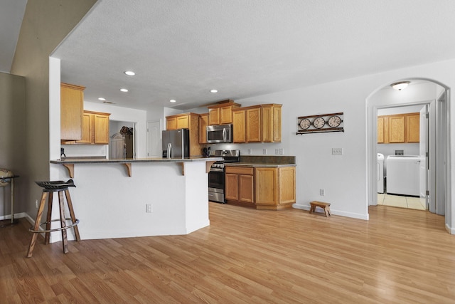 kitchen featuring arched walkways, a peninsula, appliances with stainless steel finishes, a breakfast bar area, and light wood finished floors